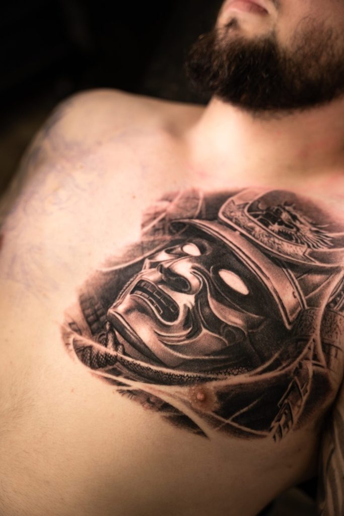Black and grey realism samurai mask chest tattoo by The KCHN Tattoos, Scarborough